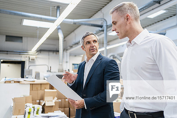 Zwei Geschäftsleute mit Papier im Gespräch in einer Fabrik