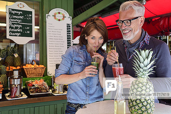 Porträt eines glücklichen reifen Paares  das an einem Marktstand einen gesunden Saft trinkt