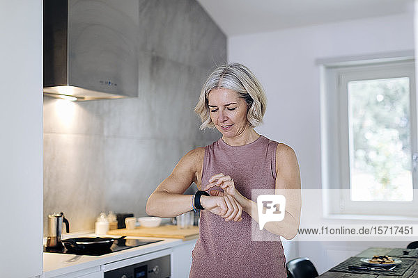 Reife Frau benutzt Smartwatch in der Küche zu Hause