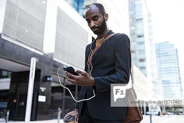 Junger Geschäftsmann betrachtet Smartphone im Freien