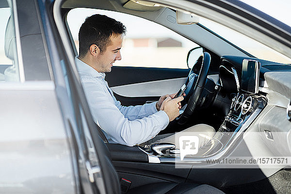 Smiling young businessman using smartphone in car
