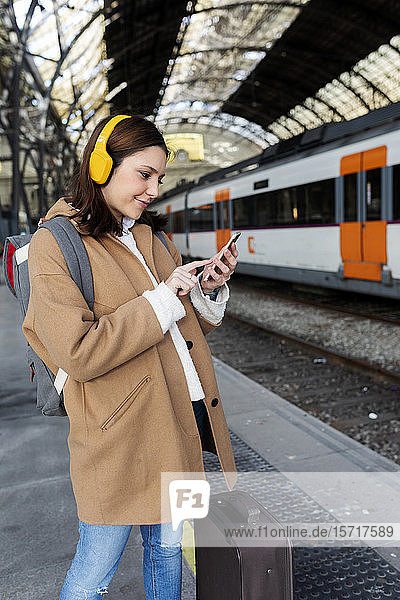 Junge Frau mit Kopfhörern und Handy am Bahnhof