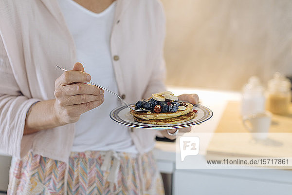 Close-up of woman holding a plate with pancakes and fruit