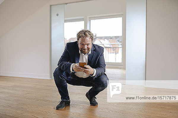 Porträt eines lächelnden Immobilienmaklers mit Smartphone in einer leeren Wohnung