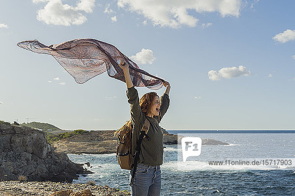 Happy redheaded young woman holding a cloth at the coast Ibiza Spain