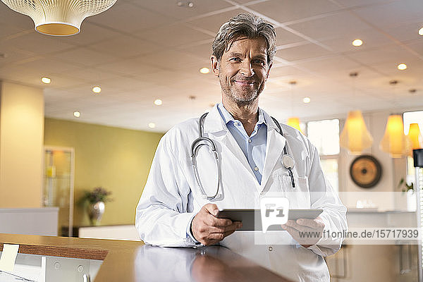 Porträt eines selbstbewussten Arztes mit Tablette beim Empfang in seiner Arztpraxis