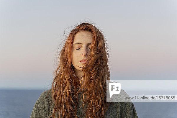 Rothaarige junge Frau mit geschlossenen Augen bei Sonnenuntergang an der Küste  Ibiza  Spanien