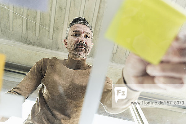 Reifer Geschäftsmann arbeitet an Haftnotizen auf Glastisch im Büro