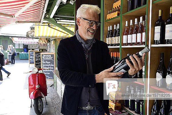 Smiling mature man choosing bottle of wine at a wine shop