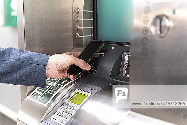 Mann hält Smartphone am Fahrkartenautomaten und bezahlt