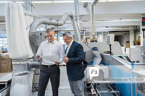 Two smiling businessmen discussing paper in a factory