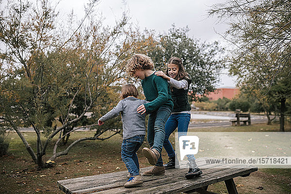 Three children dancing on picnic table in autumn having fun
