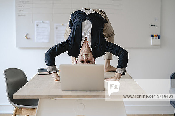 Junge Geschäftsfrau praktiziert Yoga auf dem Schreibtisch im Büro