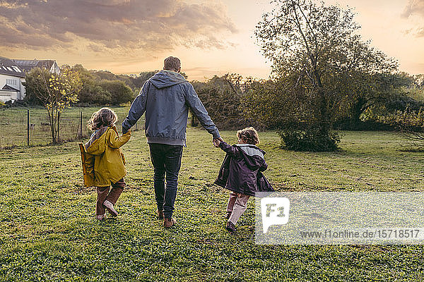 Vater mit Töchtern  die im Herbst auf einer Wiese spazieren