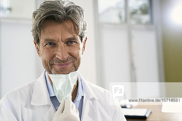 Porträt eines lächelnden Arztes mit Maske in seiner Arztpraxis