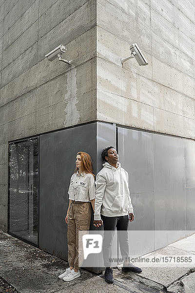 Mann und Frau lehnen an einer Wand  Überwachungskameras hängen über ihren Köpfen