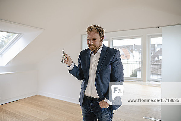 Porträt eines lächelnden Geschäftsmannes  der in einer leeren Wohnung steht und den Schlüssel hält