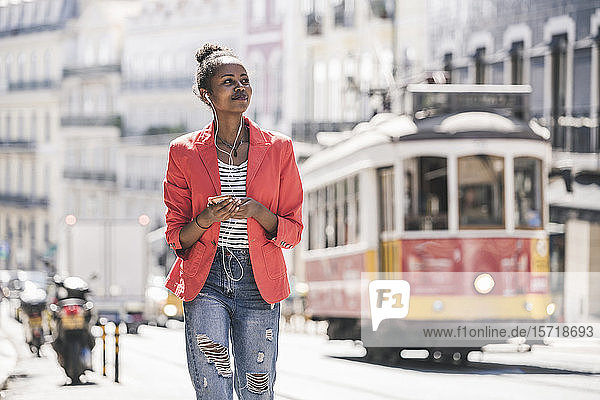 Junge Frau mit Kopfhörern und Smartphone  die sich in der Stadt umsieht  Lissabon  Portugal