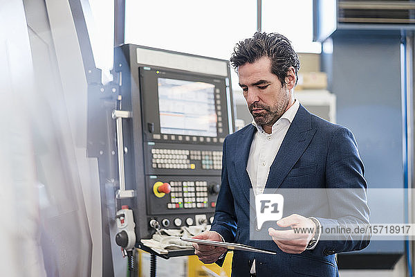 Businessman using tablet at a machine in a factory