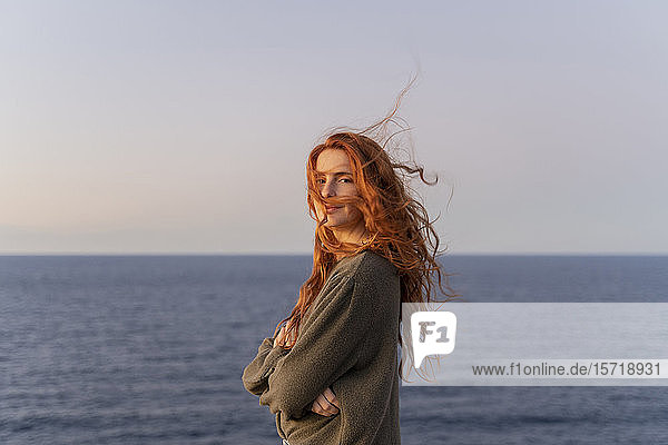 Portrait of redheaded young woman with windswept hair at the coast at sunset  Ibiza  Spain