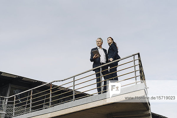 Businessman and businesswoman standing on a balcony outside office building