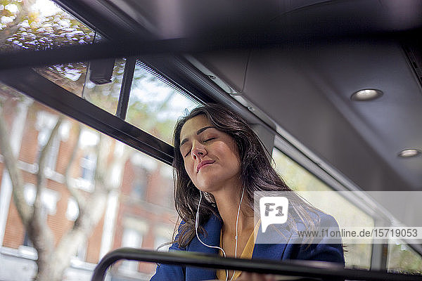 Junge Frau  die in einem Bus mit Kopfhörern und geschlossenen Augen Musik hört