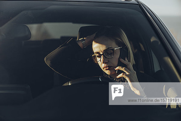 Junge blonde Geschäftsfrau mit Smartphone im Auto
