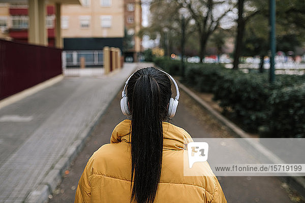 Rückenansicht einer Frau mit schwarzen Haaren  die auf der Straße mit Kopfhörern Musik hört