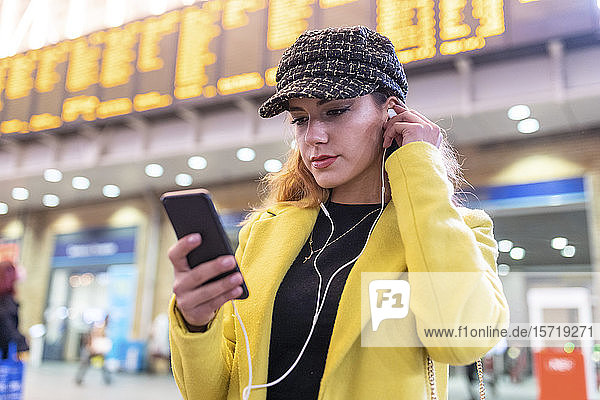 Woman at train station checking her smartphone and using earphones