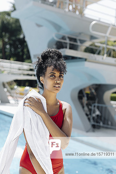 Porträt einer jungen Frau in rotem Badeanzug mit Handtüchern vor einem Pool