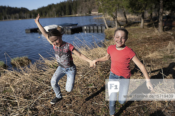 Schwestern haben Spaß am See  halten Hand  laufen und springen