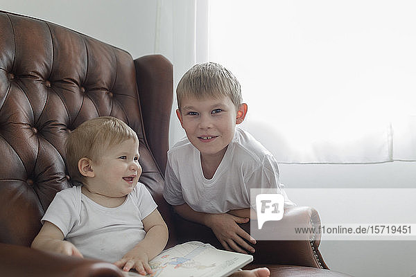 Portrait of boy with his baby brother in leather armchair in living room at home