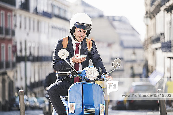 Junger Geschäftsmann auf Motorroller mit Handy in der Stadt  Lissabon  Portugal