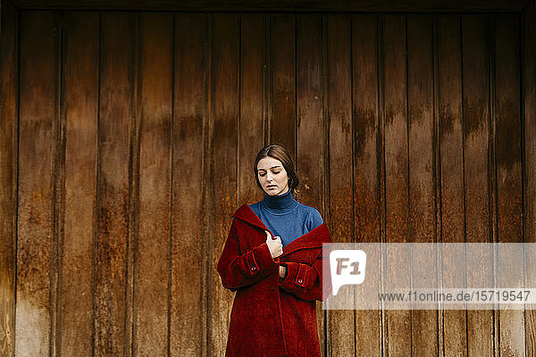 Nahaufnahme einer Frau mit blauem Rollkragenpullover und rotem Mantel vor einer Holztür