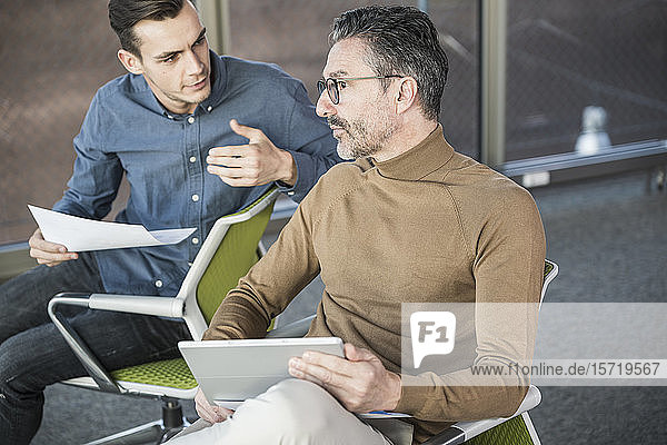 Mature businessman with tablet and young man working in office