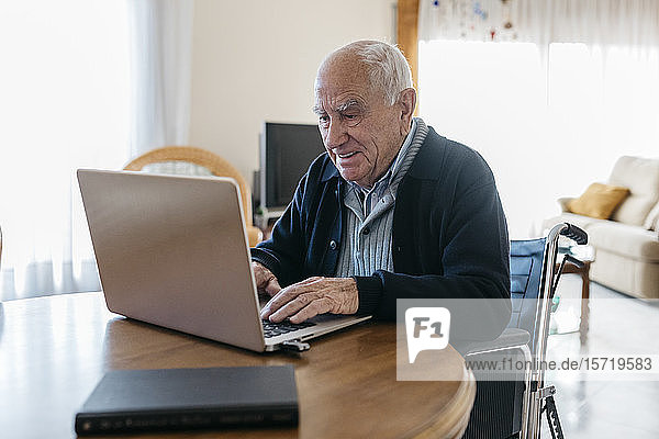 Portrait eines Seniormanns im Rollstuhl mit Laptop zu Hause