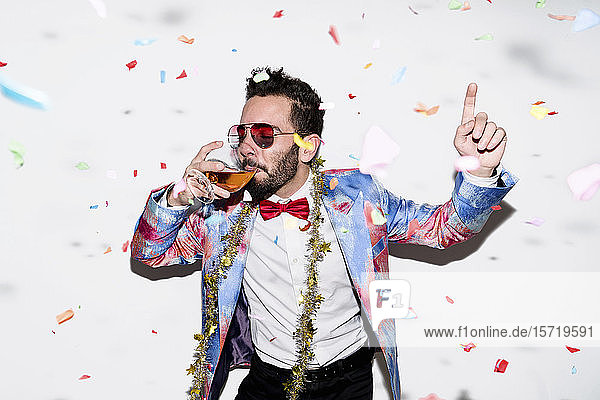 Cooler und stilvoller Mann mit farbenfrohem Anzug und Sonnenbrille feiert eine Party mit Konfetti und Trinken