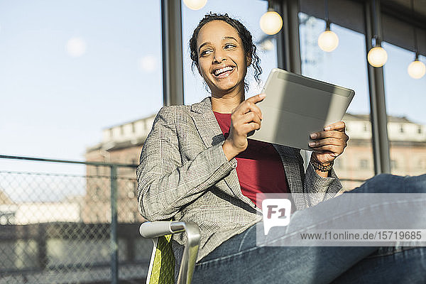 Glückliche junge Geschäftsfrau benutzt ein Tablett am Fenster im Büro