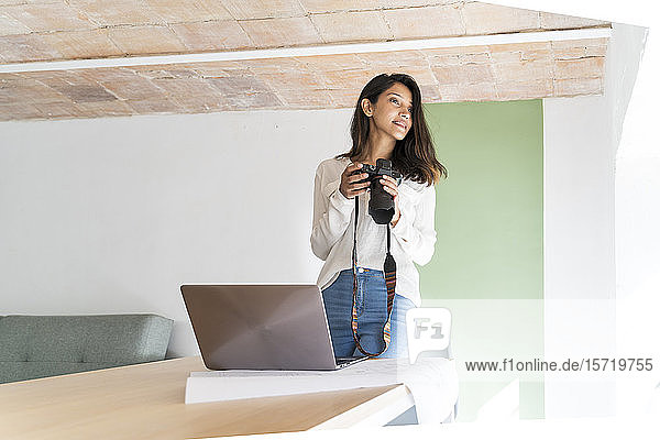 Junger Architekt mit Kamera  Laptop und Bauplan auf dem Schreibtisch im Atelier mit Blick in die Ferne