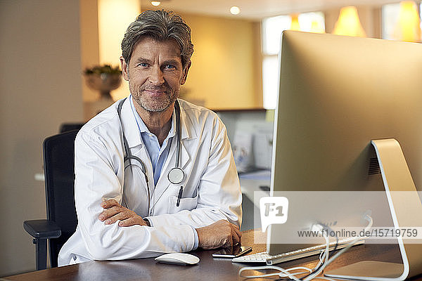 Porträt eines selbstbewussten Arztes am Schreibtisch in seiner Arztpraxis