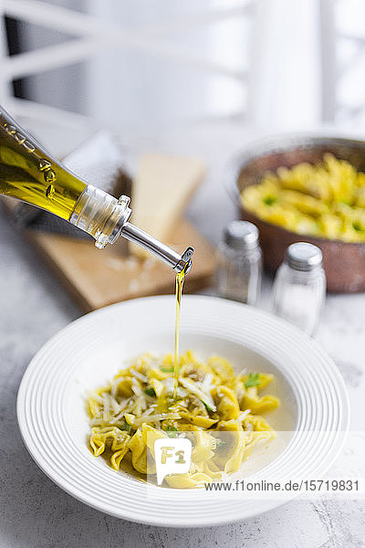 Olivenöl das in einen Teller italienische Tortellini mit Grana-Käse gegossen wird