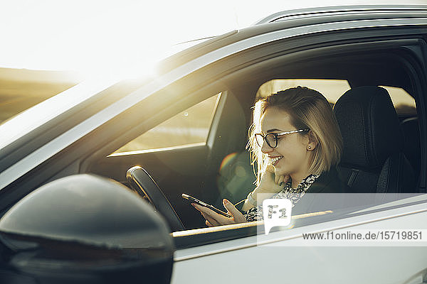 Junge blonde Frau mit Smartphone im Auto