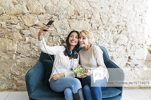 Zwei Kollegen  die mittags auf der Couch sitzen und sich mit dem Smartphone selbstständig machen