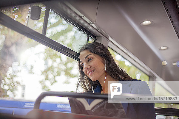 Junge Frau  die in einem Bus mit Kopfhörern Musik hört und aus dem Fenster schaut