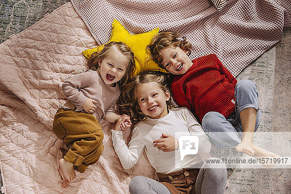Drei glückliche Mädchen liegen zu Hause auf Decken