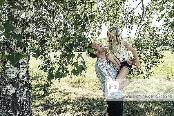 Glücklicher Vater trägt Tochter unter einer Birke