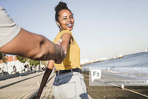 Happy young woman holding hand of her boyfriend on pier at the waterfront  Lisbon  Portugal
