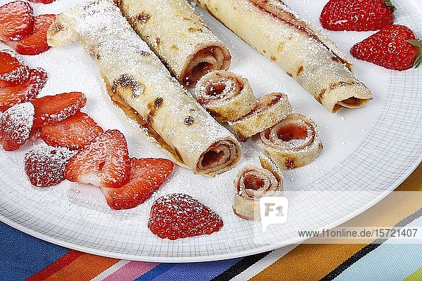 Dessert  gefüllte Pfannkuchen mit Marmelade  Puderzucker und frischen Erdbeeren  gerollt auf einem Teller  Deutschland  Europa