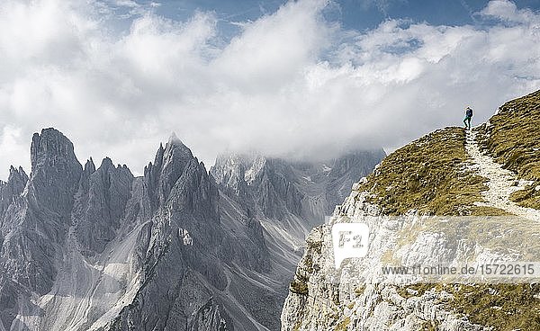 Junge Frau  Bergsteigerin auf einem Wanderweg  hinter Bergspitzen und scharfen Felsgipfeln  bewölkter Himmel  Cimon di Croda Liscia und Cadini-Gruppe  Sextner Dolomiten  Belluno  Italien  Europa