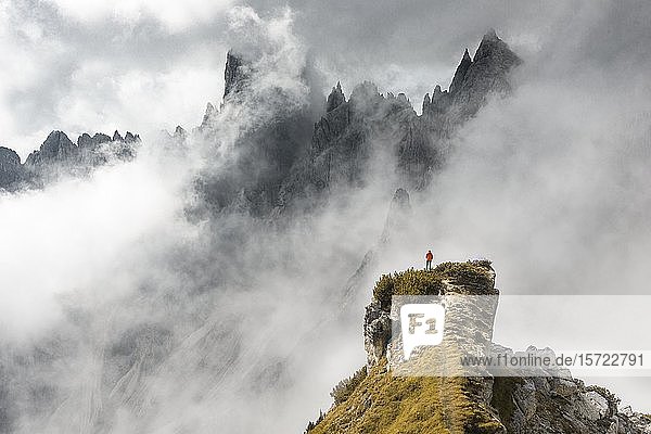 Bergsteiger steht auf einem Bergrücken  hinter Bergspitzen und spitzen Felsen  dramatische Wolken  Cimon di Croda Liscia und Cadini-Gruppe  Auronzo di Cadore  Belluno  Italien  Europa